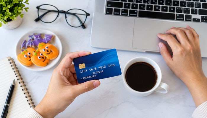 Who Should Consider a No-Fee or Low-Fee Prepaid Card? - Startup Editor | Startup Editor Person holding a payment card near a laptop while researching Prepaid Cards With No Fees for online purchases and everyday spending.