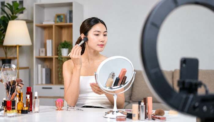 Higossis Brush Cons for Concealer - Startup Editor | Startup Editor Is Higossis Brush Good for Concealer – woman using a makeup brush in front of a vanity mirror and ring light with cosmetics arranged nearby.