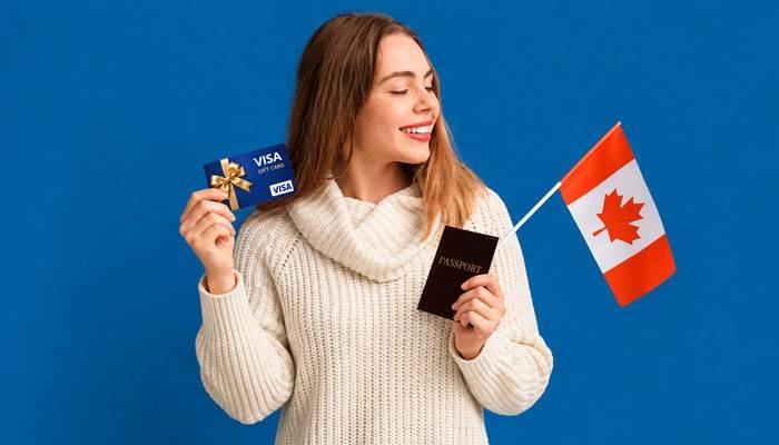 Can You Use a Visa Gift Card in Canada? - Startup Editor | Startup Editor Can Visa Gift Cards Be Used Internationally? Woman holding a Visa gift card, passport, and Canadian flag while exploring payment options for travel to Canada.